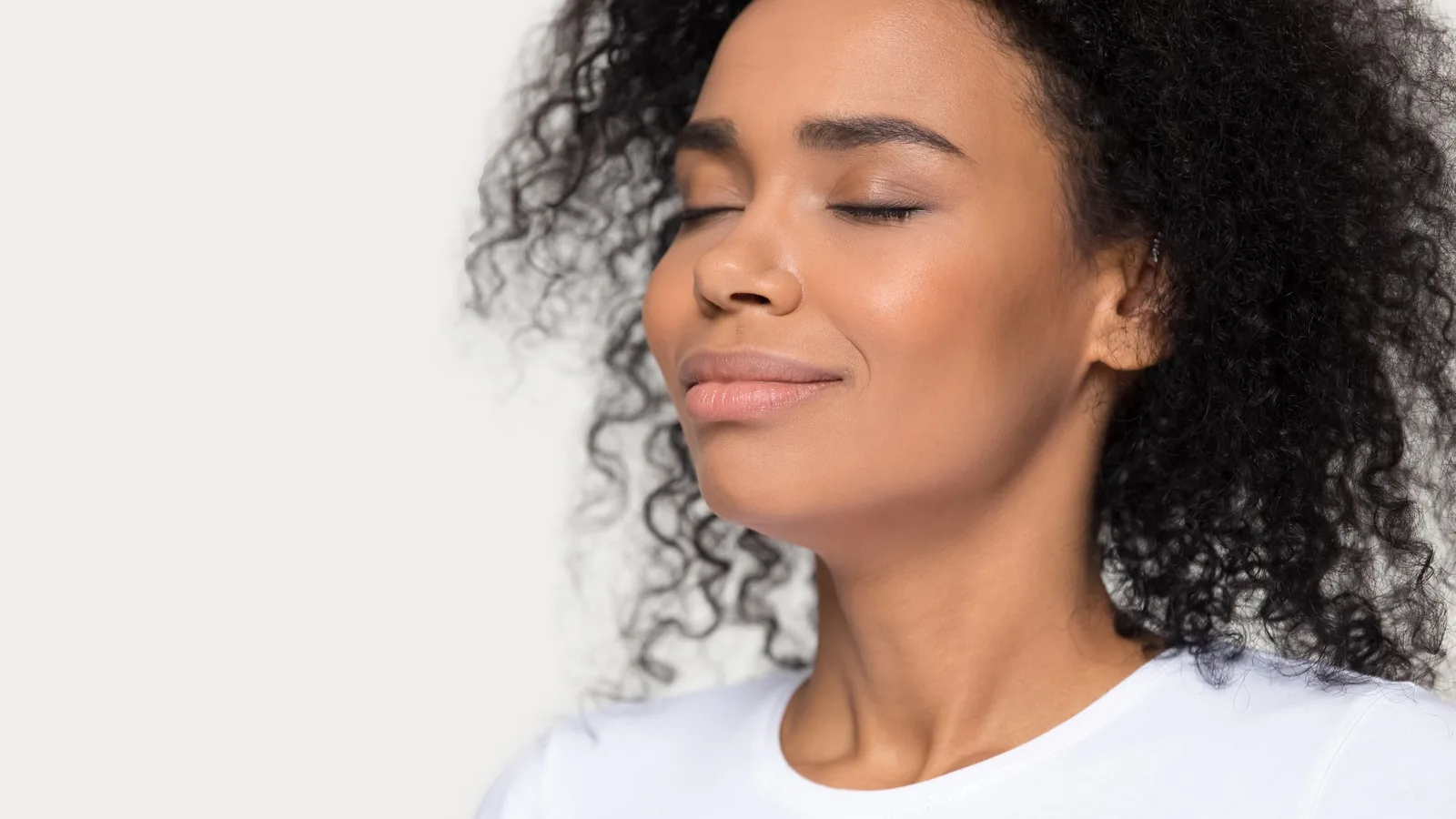 A woman with her eyes closed and head tilted back, mid exhale, against a plain background