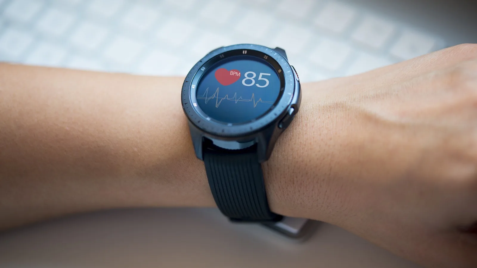 A smartwatch on a wrist displaying a heart icon and a reading of 85 beats per minute