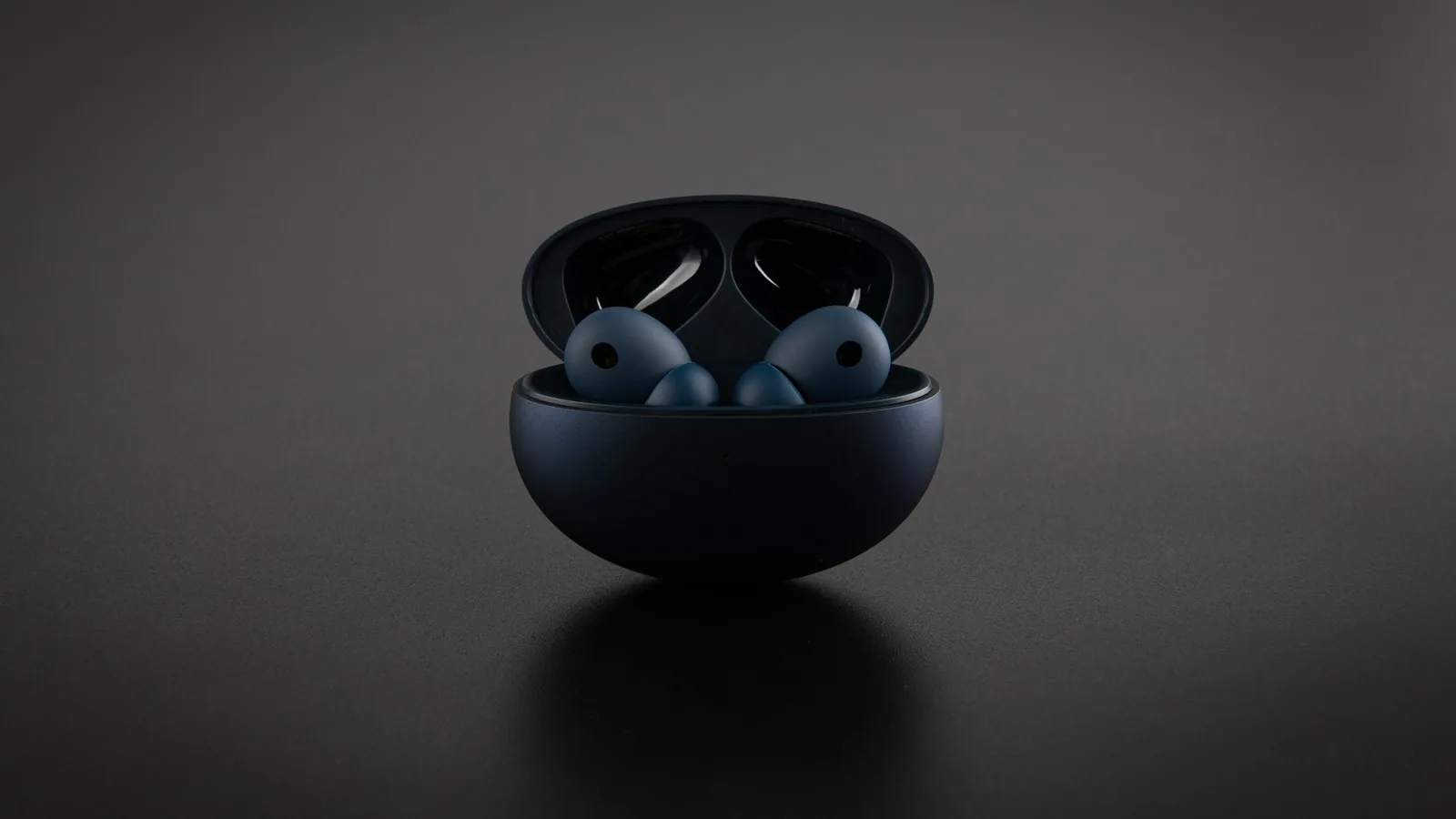 A pair of dark wireless earbuds in an open charging case on a matte black surface