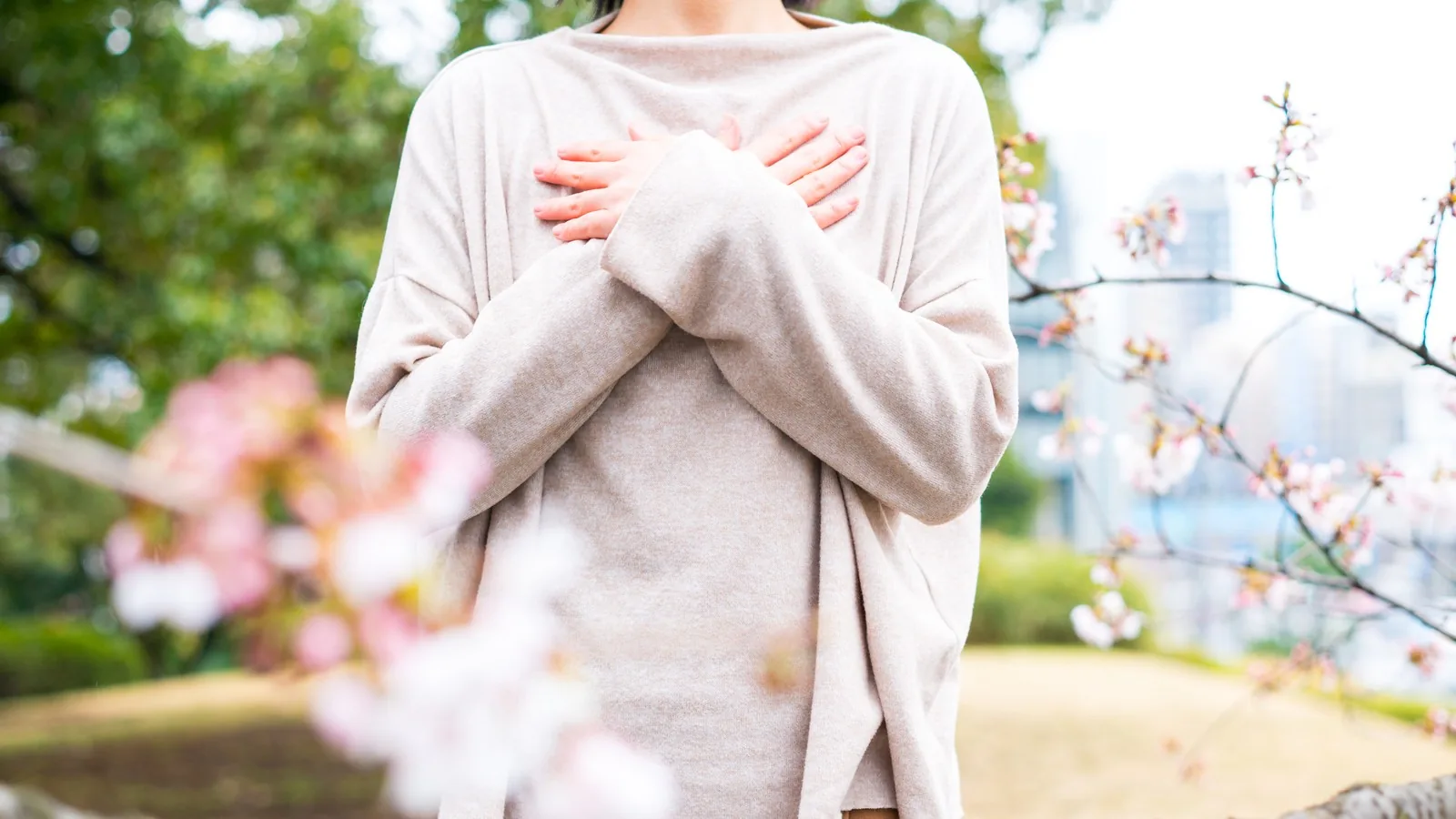 A person standing outdoors among blossom with both hands resting on their chest, breathing slowly